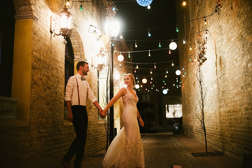 Bride and groom from Chicago kissing under twinkly lights in a brick alleyway.