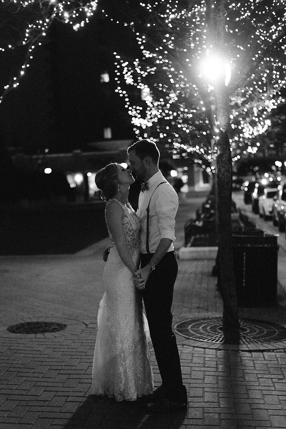Black and white photo of bride and groom from Chicago kissing under twinkly lights in a brick alleyway.
