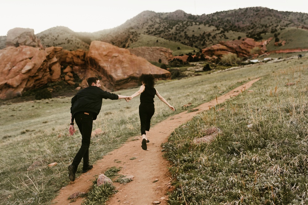 couple running through trails at red rock ampitheatre colorado