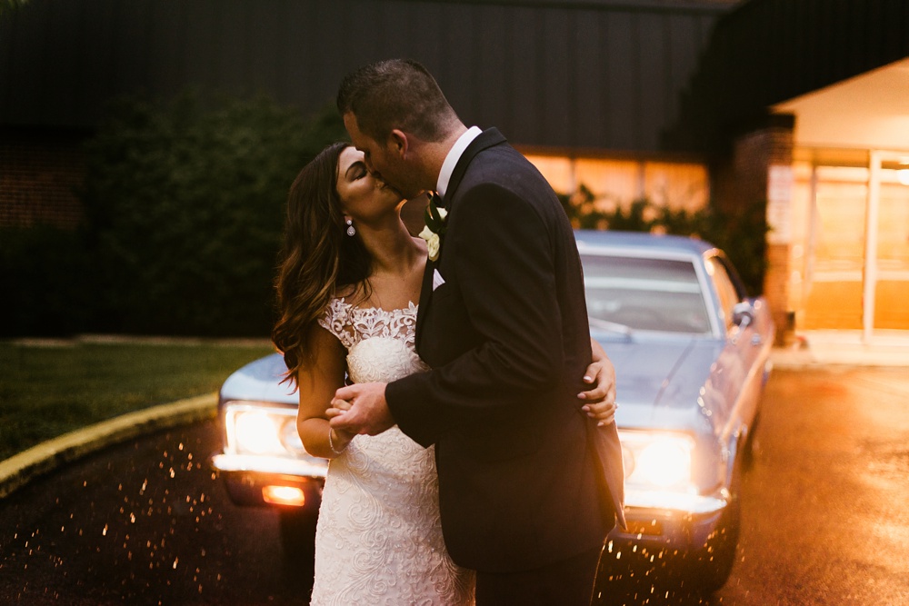 bride and groom dancing in rain in front of vintage car