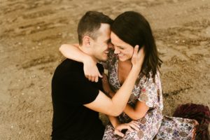 couple sitting in sand and embracing during engagement session at france park
