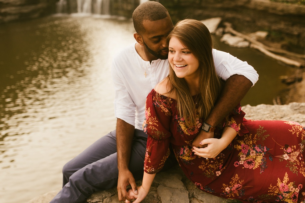 couple sitting in front of waterfall during engagement session at cataract falls