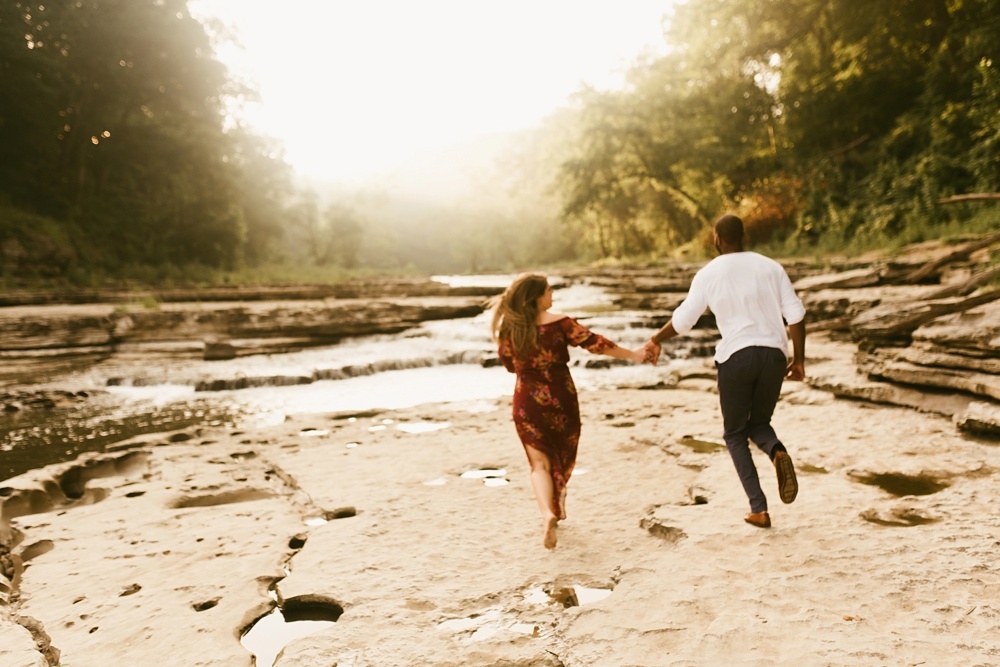 couple running across beach during engagement session at cataract falls
