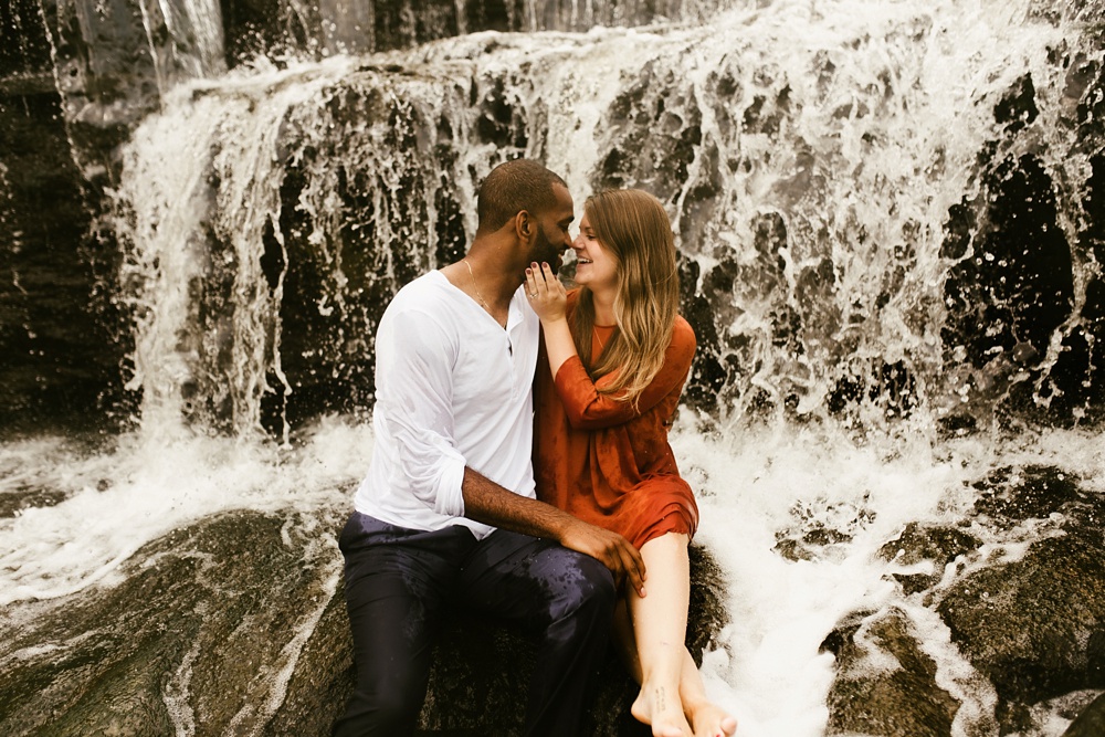 couple playing in waterfall during engagement session at cataract falls