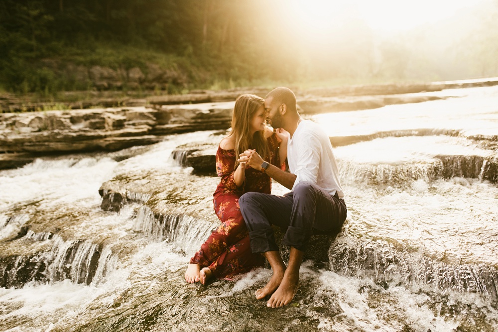 couple sitting in waterfall during engagement session at cataract falls