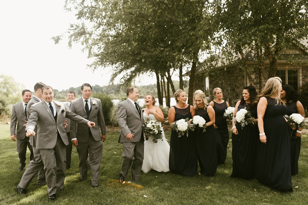 bridal party in navy dresses and gray tuxes laughing with bride and groom bridal party