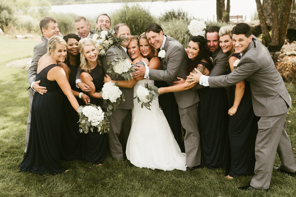 bridal party in gray tuxes and navy dresses hugging couple at at glendarin golf course