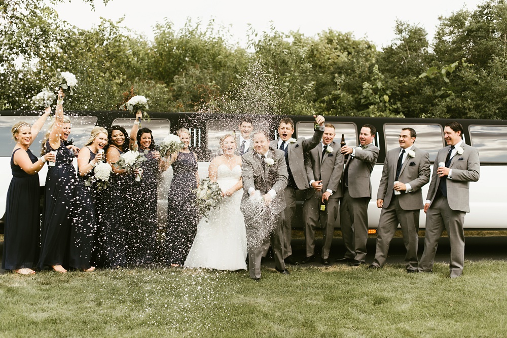 bridal party in gray tuxes and navy dresses with couple popping champagne at glendarin golf course