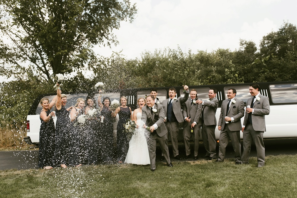 bridal party in gray tuxes and white dresses with couple popping bottle of champagne at glendarin golf course