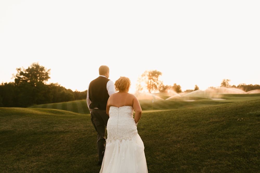 bride and groom holding hands in field during sunset at glendarin golf course