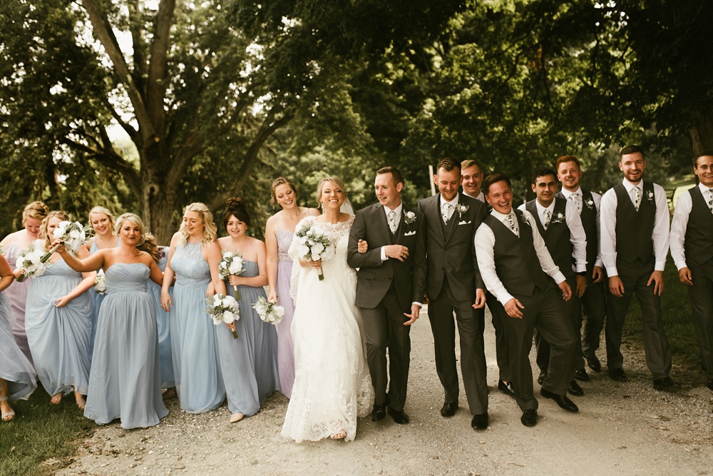wedding party in pastel dresses and gray tuxes walking bride and groom at j weaver barn wedding