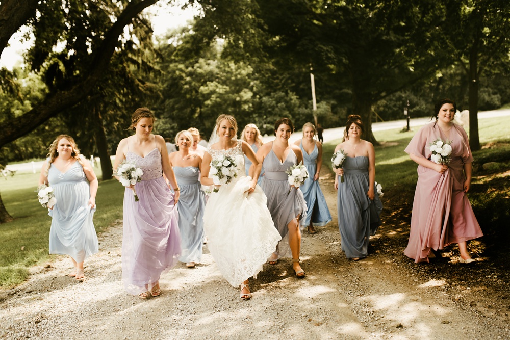 bridal party in pastel dresses walking with bride at j weaver barn wedding