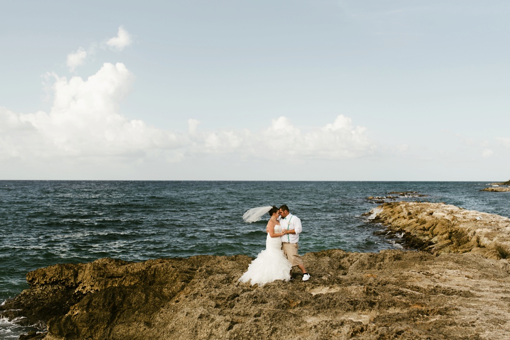 bride and groom hugging on oceanside rocks at grand palladium jamaica wedding