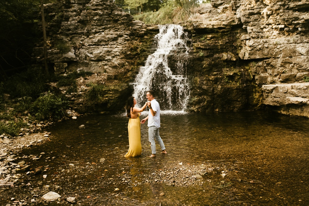 couple holding hands in water at indiana waterfall engagement photoshoot