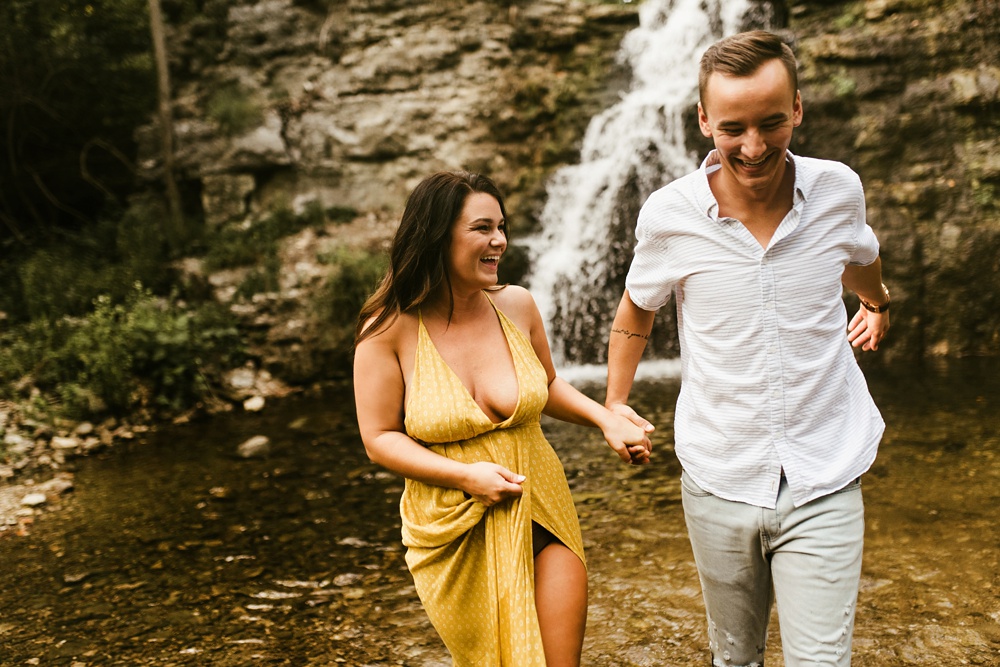couple holding hands and laughing at indiana waterfall engagement photoshoot