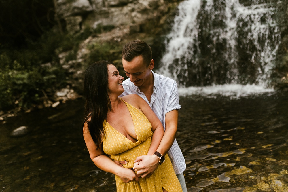 couple smiling at each other by water at indiana waterfall engagement photoshoot