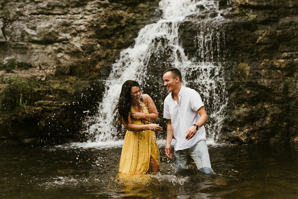 couple laughing and splashing in water at indiana waterfall engagement photoshoot