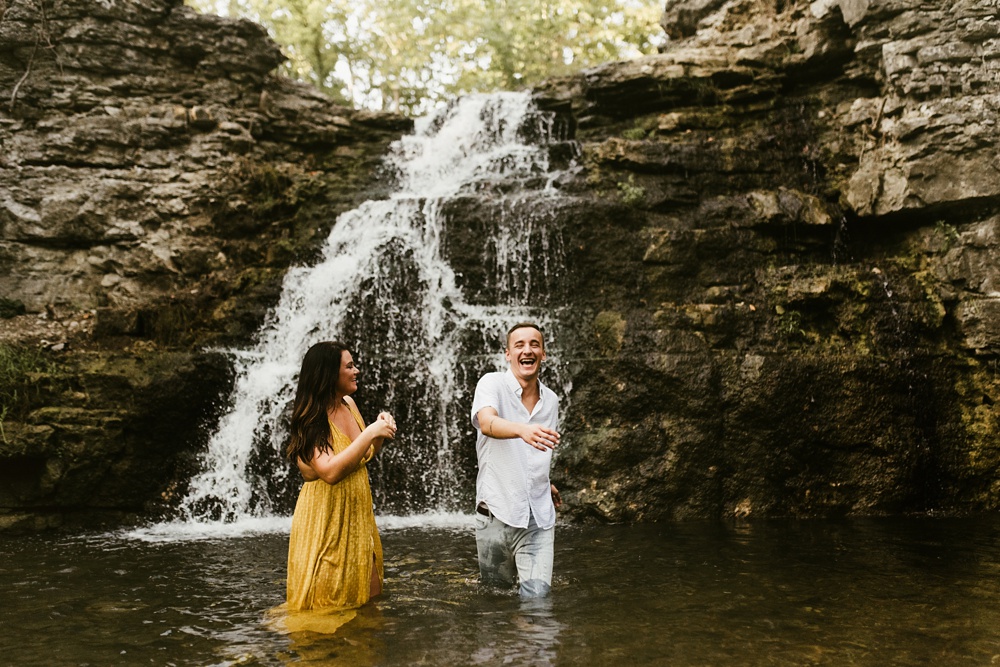 couple laughing and splashing in water at indiana waterfall engagement photoshoot