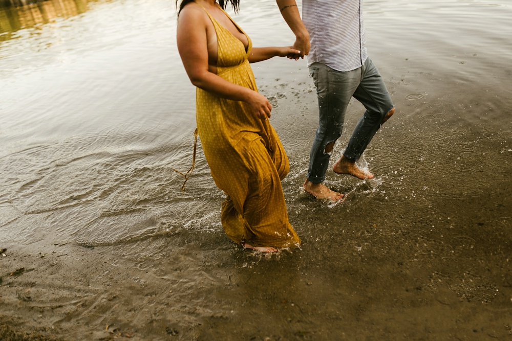 couple holding hands and splashing in lake at indiana waterfall engagement photoshoot