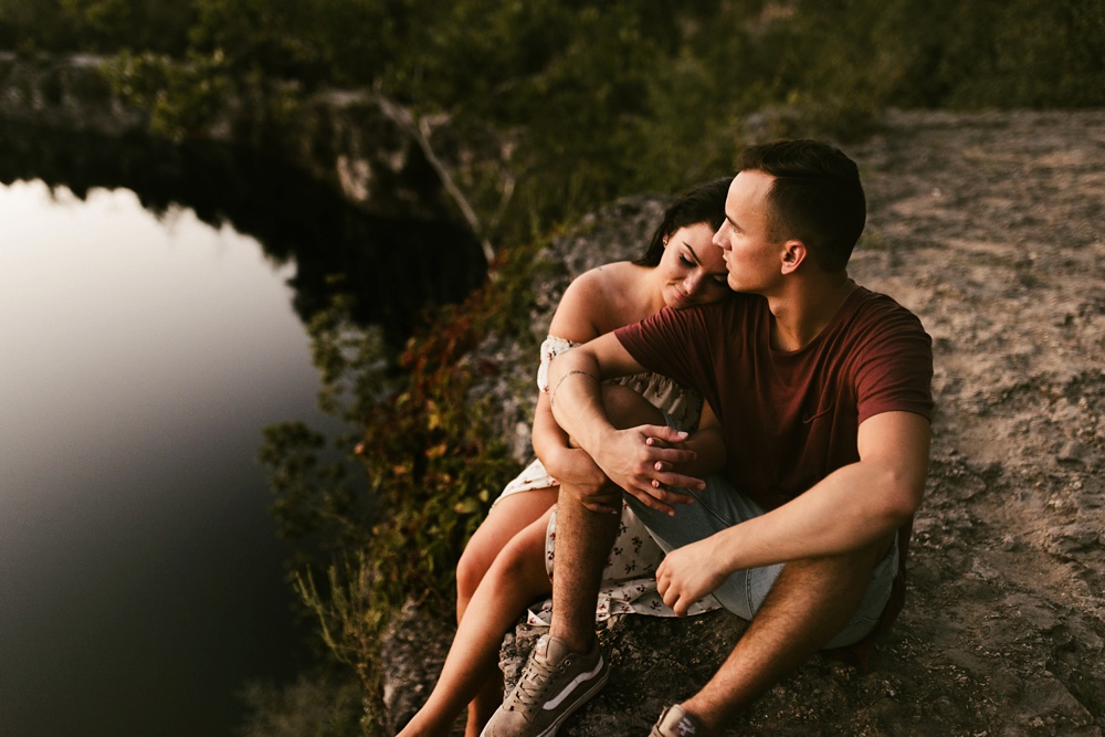 coupld sitting on cliff overlooking lake at indiana waterfall engagement photoshoot