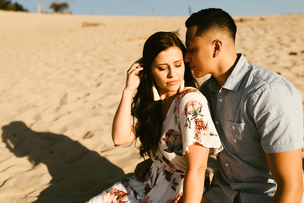 couple sitting on sand at dune at warren dunes state park engagement session
