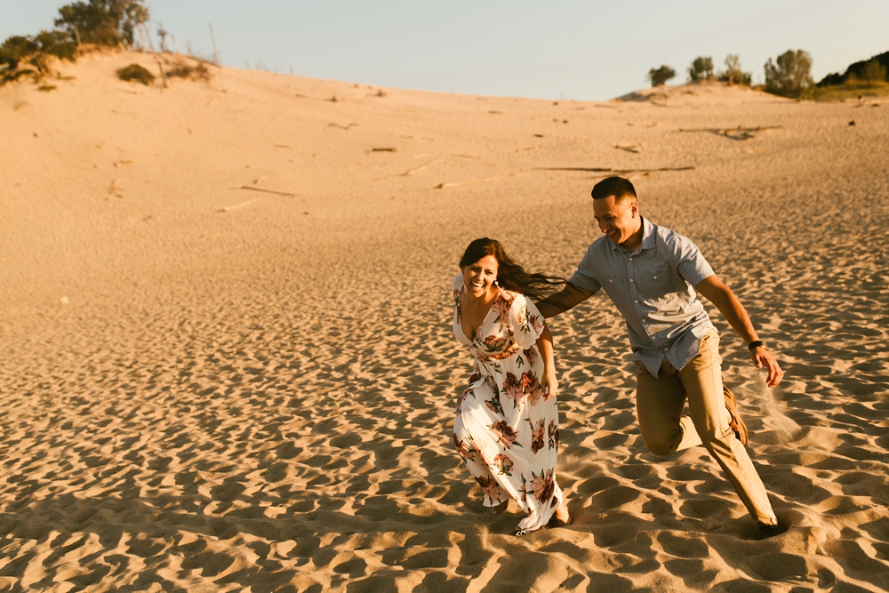couple smiling and running at dune at warren dunes state park engagement session