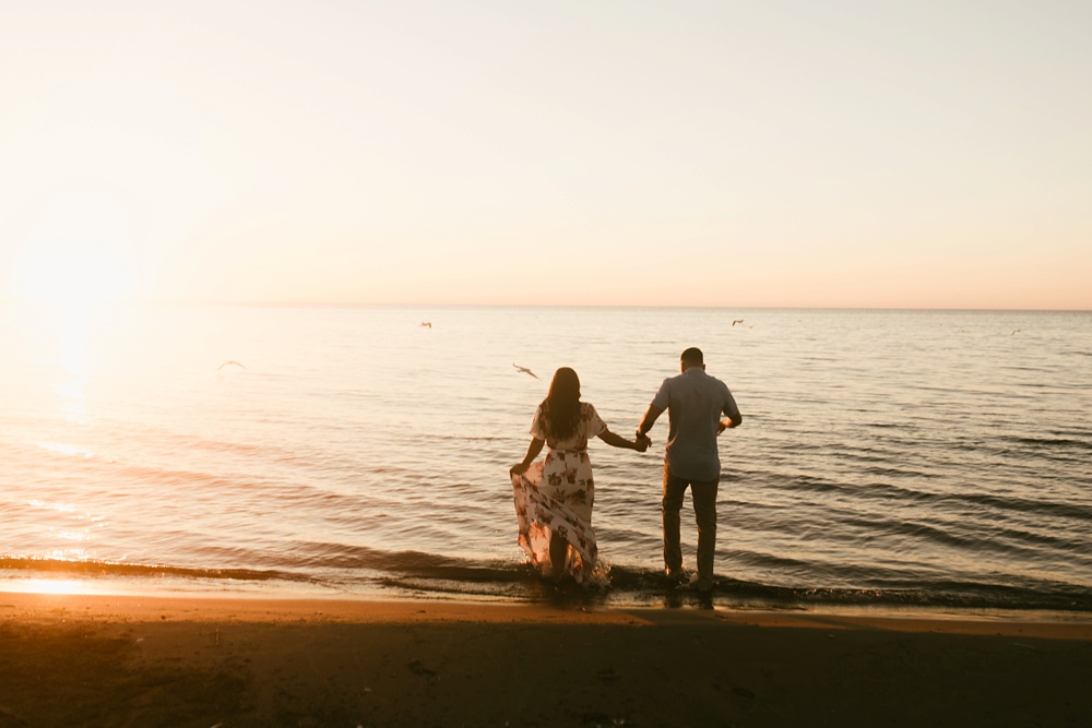 couple wading into water at sunset at dune at warren dunes state park engagement session