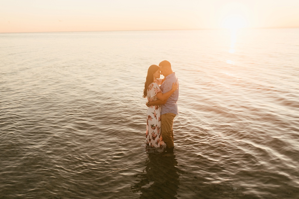 couple hugging in water at sunset at dune at warren dunes state park engagement session