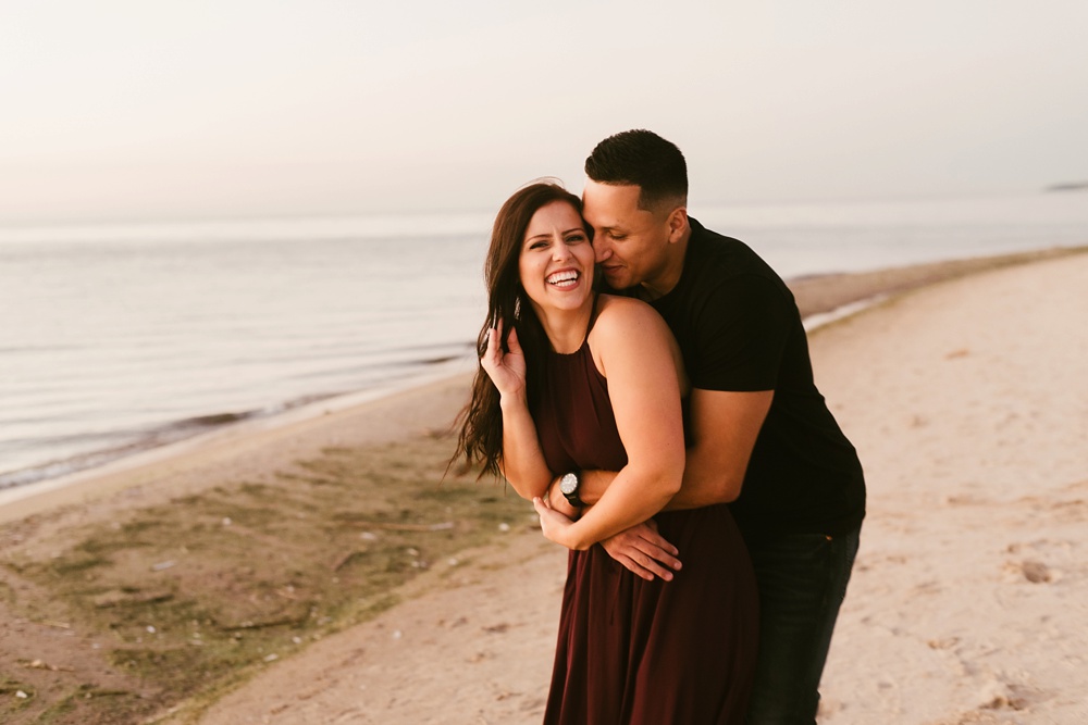 couple hugging and laughing on beach at dune at warren dunes state park engagement session