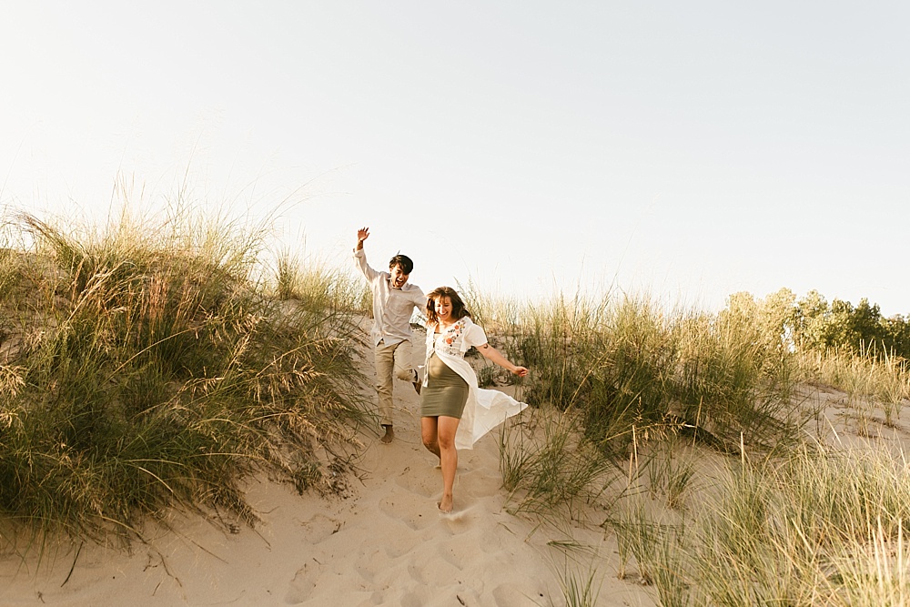 couple running down sand dune at warren dunes van life engagement shoot