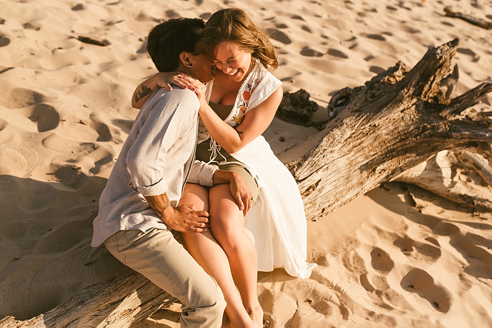 couple sitting on fallen tree laughing at warren dunes van life engagement shoot