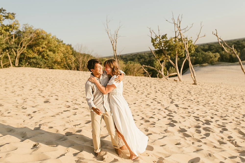 couple laughing on sand dune at warren dunes van life engagement shoot