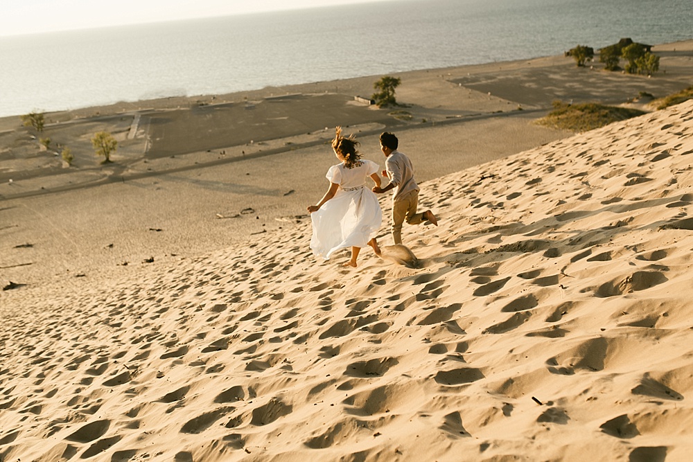 couple holding hands running down dune at warren dunes van life engagement shoot