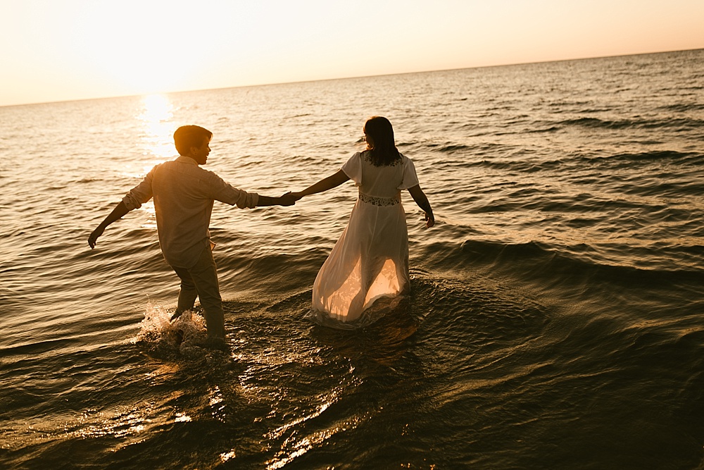 couple holding hands in water at warren dunes van life engagement shoot