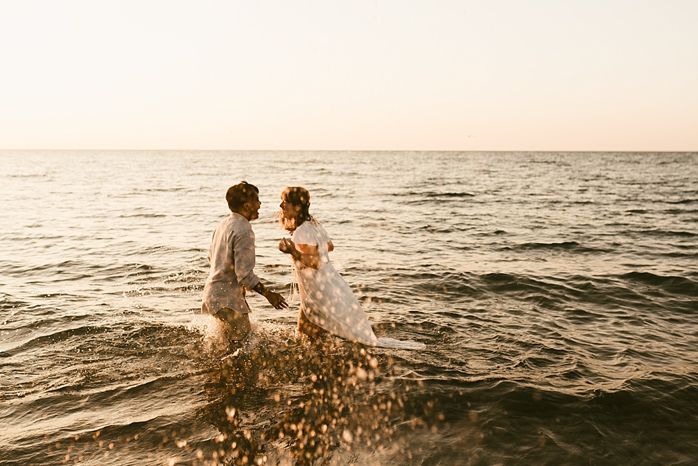 couple running through water at warren dunes van life engagement shoot
