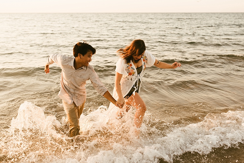couple running through water at warren dunes van life engagement shoot