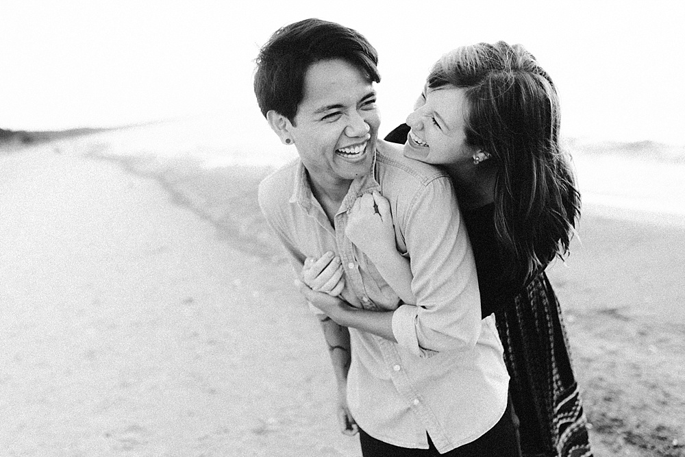 couple laughing on beach at warren dunes van life engagement shoot