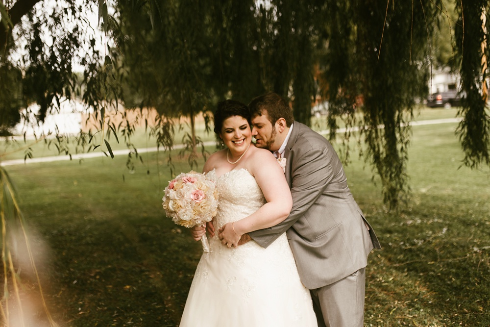 groom kissing bride under willow tree at foster park wedding photos