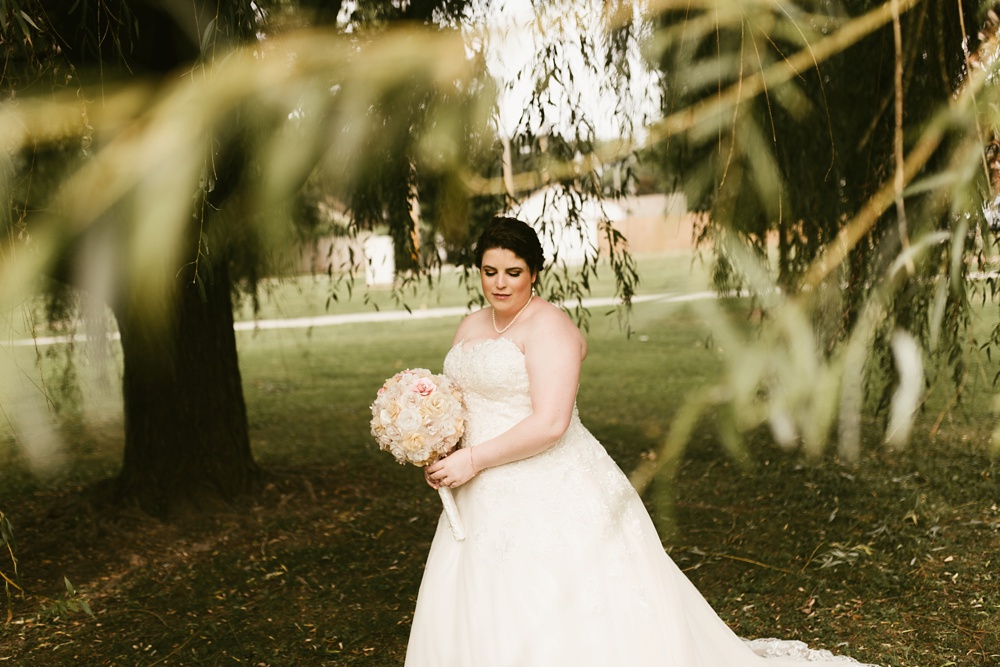 bride standing with bouquet under willow tree at foster park wedding photos