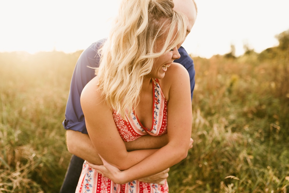 couple hugging by field at sunset at eagle marsh nature preserve engagement session
