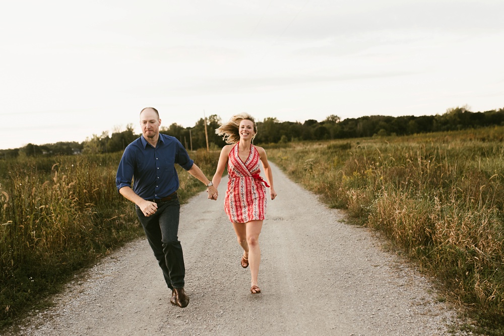 couple holding hands down road by field at eagle marsh nature preserve engagement session