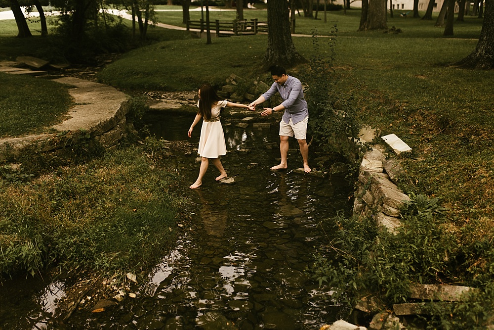 couple holding hands crossing creek on campus at indiana university bloomington engagement session