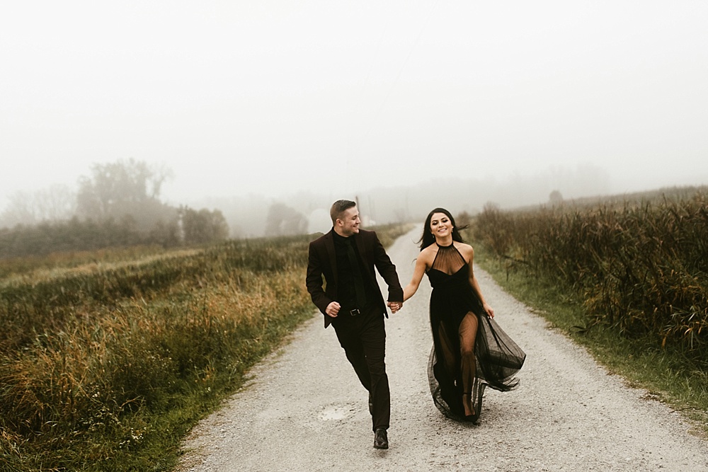 couple holding hands running down foggy path at sunrise eagle marsh engagement session