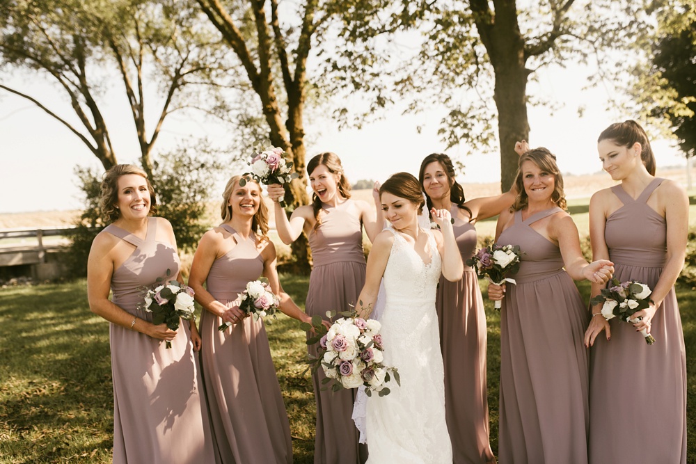 bridal party posing and laughing in rose dresses at indiana wesleyan fairmount campground wedding