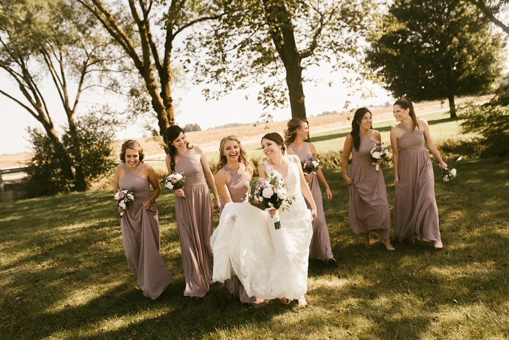 bridal party walking and laughing in rose dresses at indiana wesleyan fairmount campground wedding