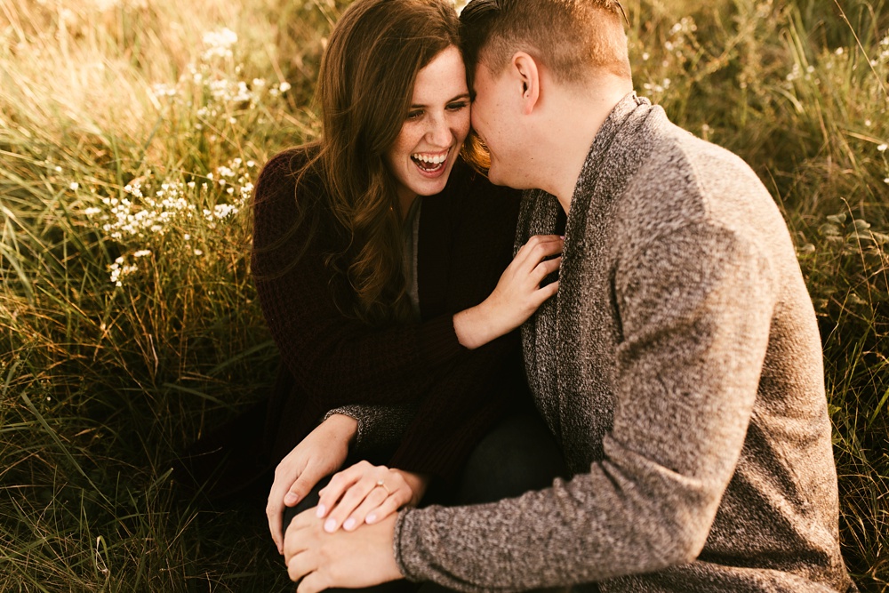 couple laughing sitting in field at golden hour fort wayne autumn engagement session