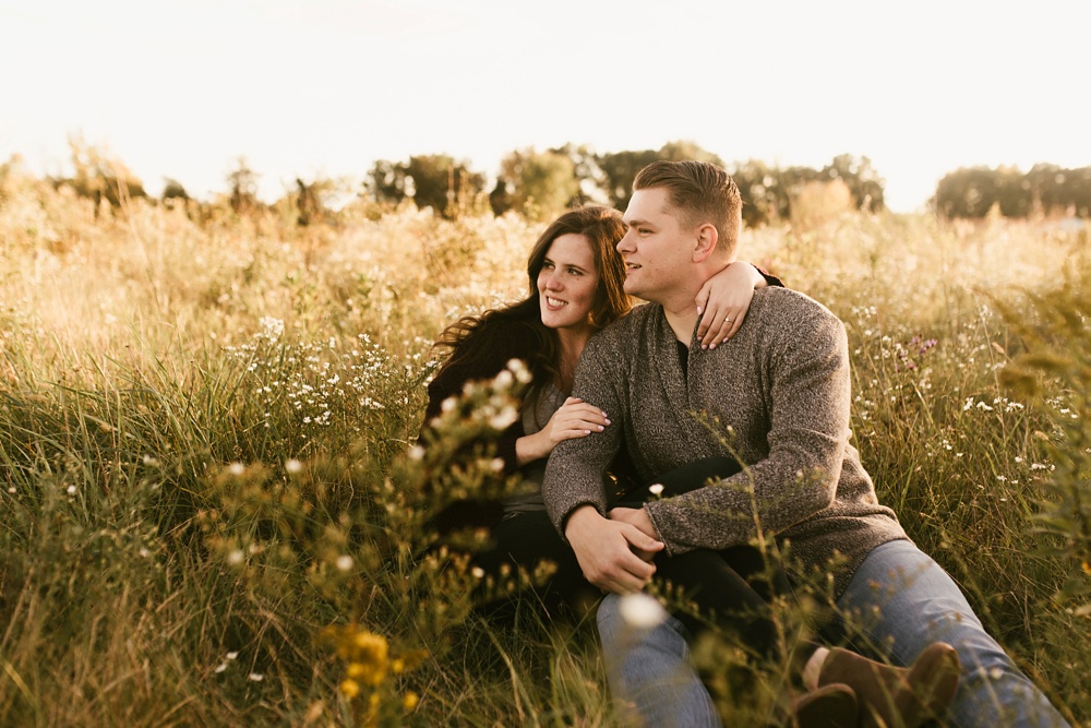 couple with arms around each other sitting in field at golden hour fort wayne autumn engagement session