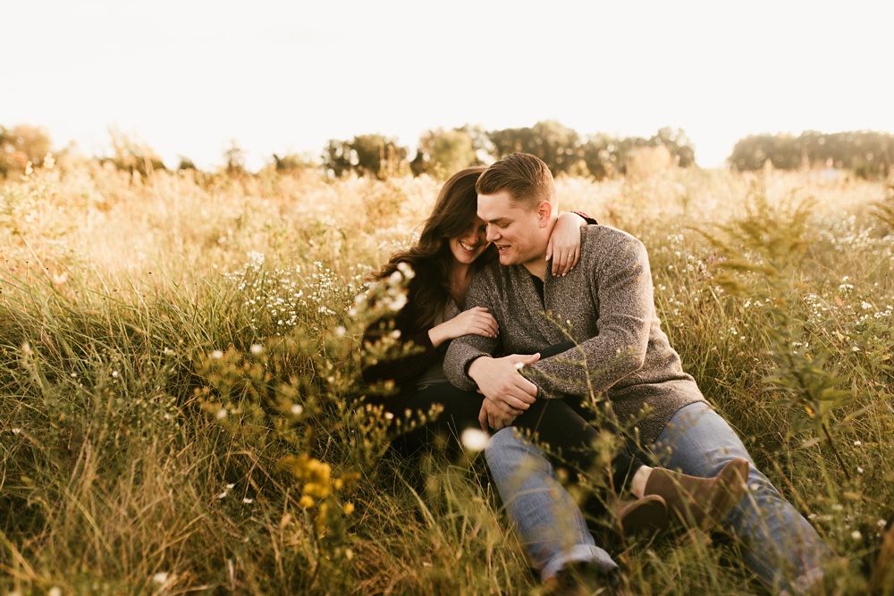 couple smiling sitting in field at golden hour fort wayne autumn engagement session