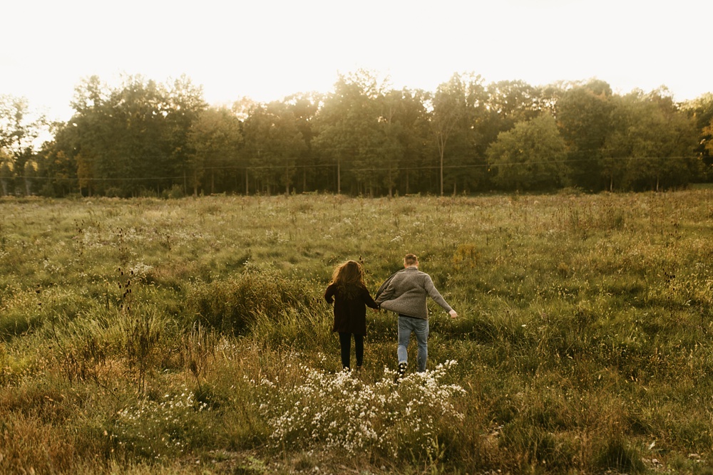 couple running through field in field at golden hour fort wayne autumn engagement session