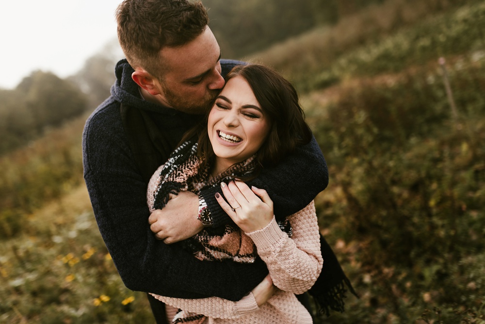 couple kissing and laughing in field at auburn sunrise engagement session